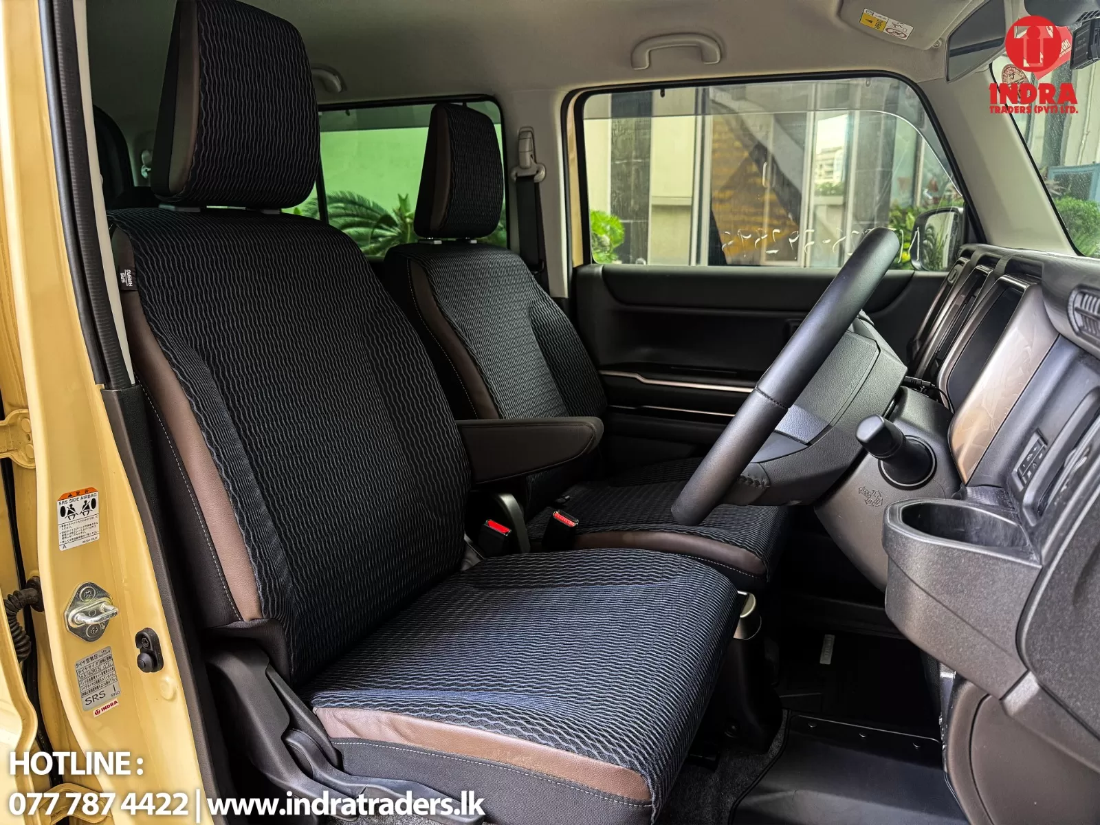 Interior of a right-hand-drive vehicle showing front seats, steering wheel, and dashboard with a yellow door frame visible at the edge.