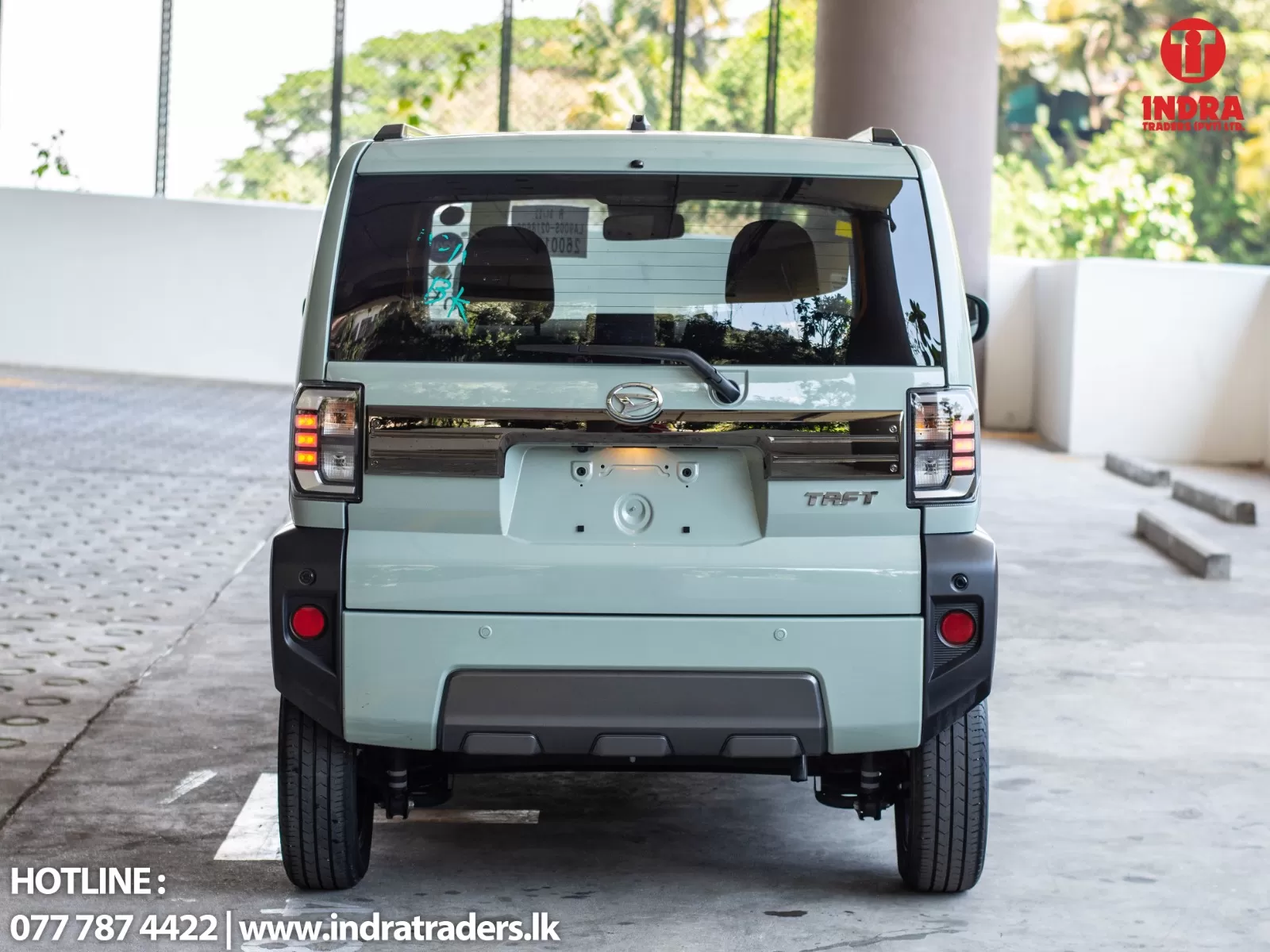 Rear view of a light-blue Daihatsu Taft SUV parked in a lot; Indra Traders logo at top-right and contact line at bottom-left.