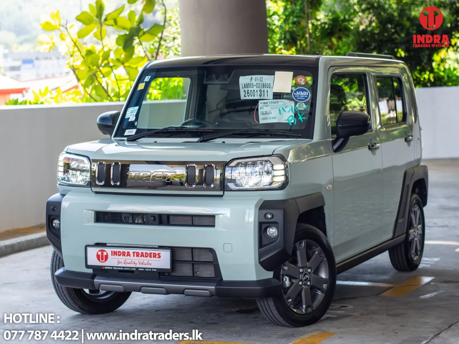 Three-quarter front view of a light blue SUV parked indoors with Indra Traders branding on the license plate and a red logo in the top-right corner.