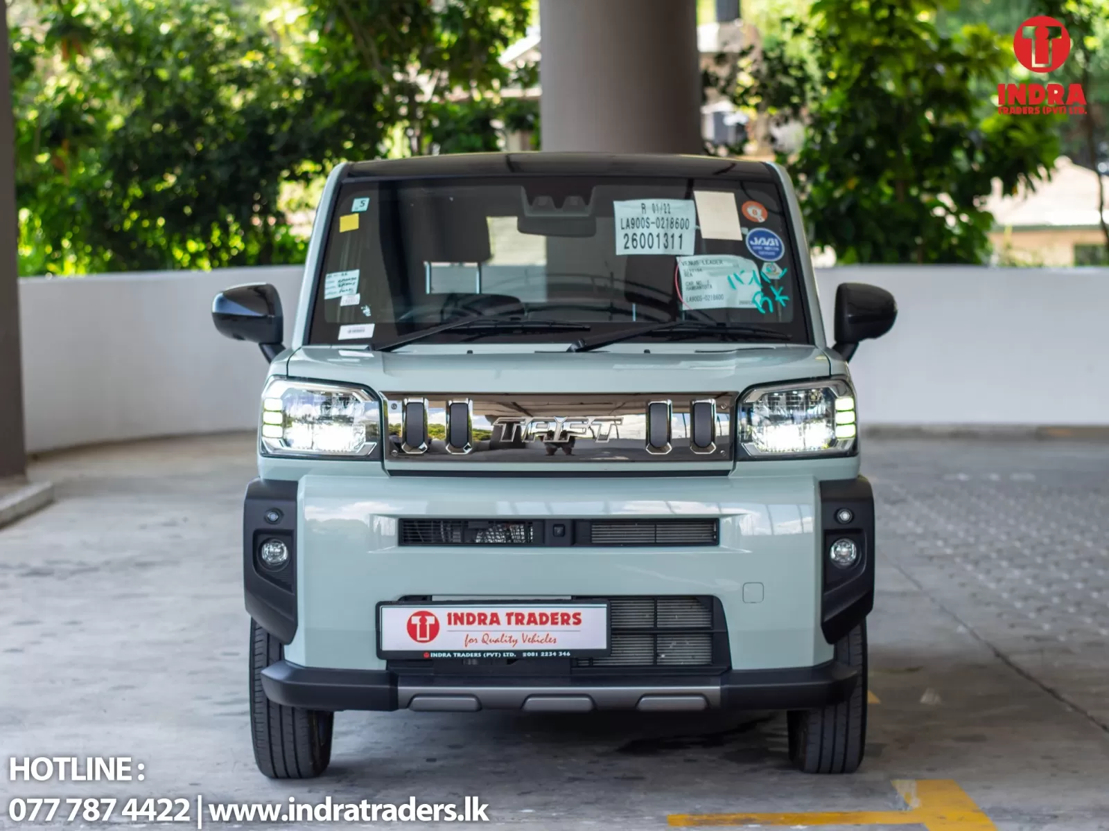 Front view of a white SUV facing the camera, with Indra Traders branding on the windshield and a cluster of stickers, parked in a covered area.
