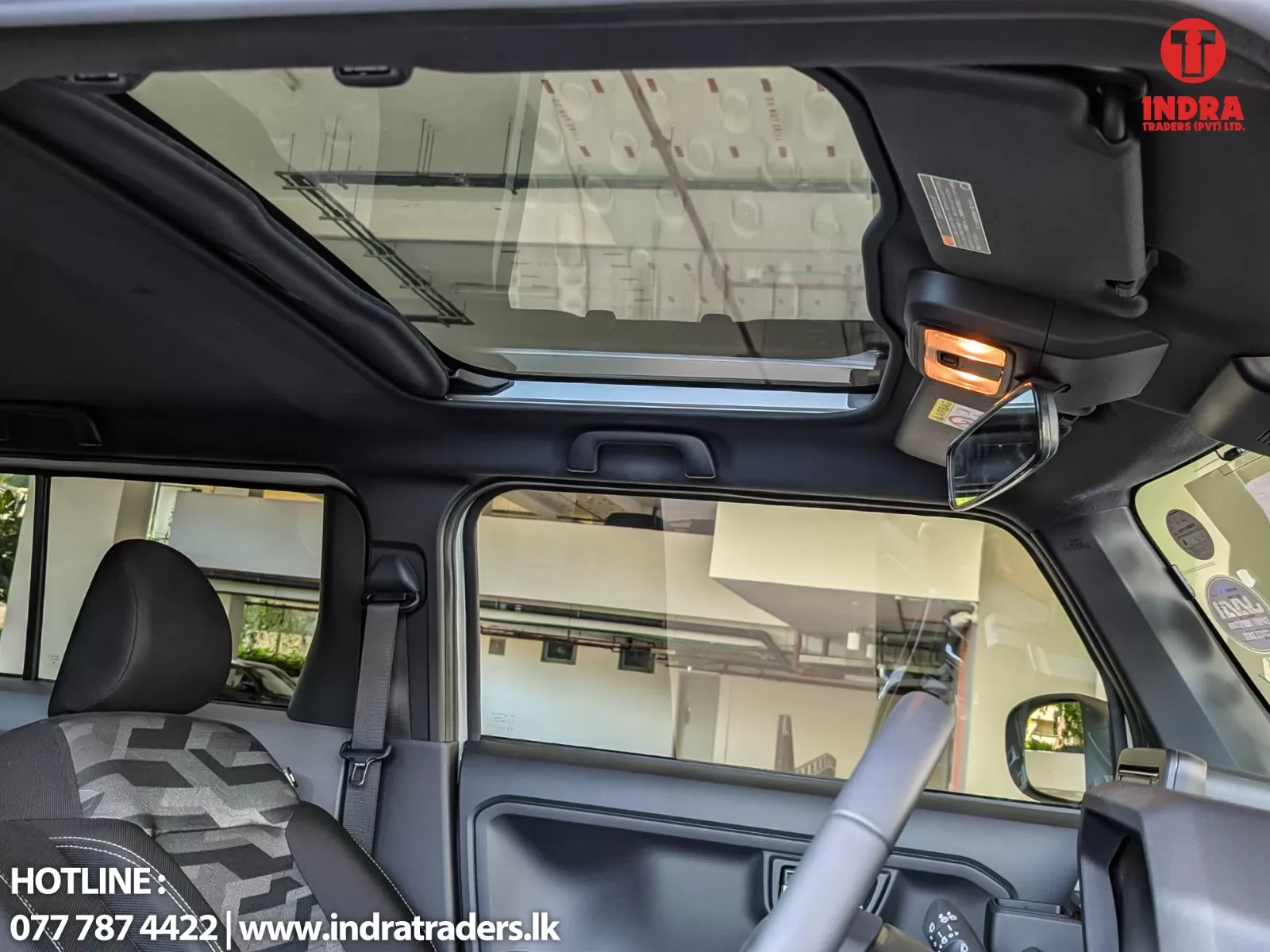 Interior of a car showing a large glass sunroof, overhead console and a pair of sunglasses hanging near the mirror; branding watermark in corner.