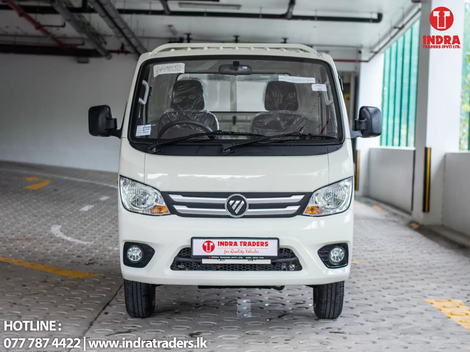 Front view of a white van in a showroom with Indra Traders branding on the license plate and corner logo
