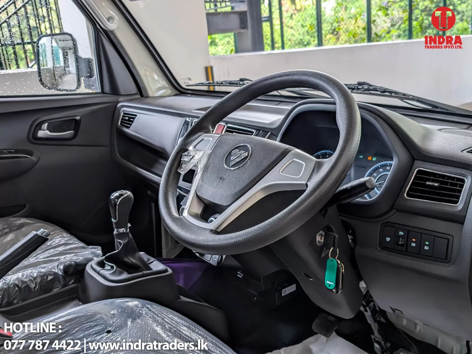 Interior of a left-hand drive car showing the steering wheel, dashboard, and gear shifter in the foreground. A plastic cover is on the seat and the windshield wipers are visible outside.