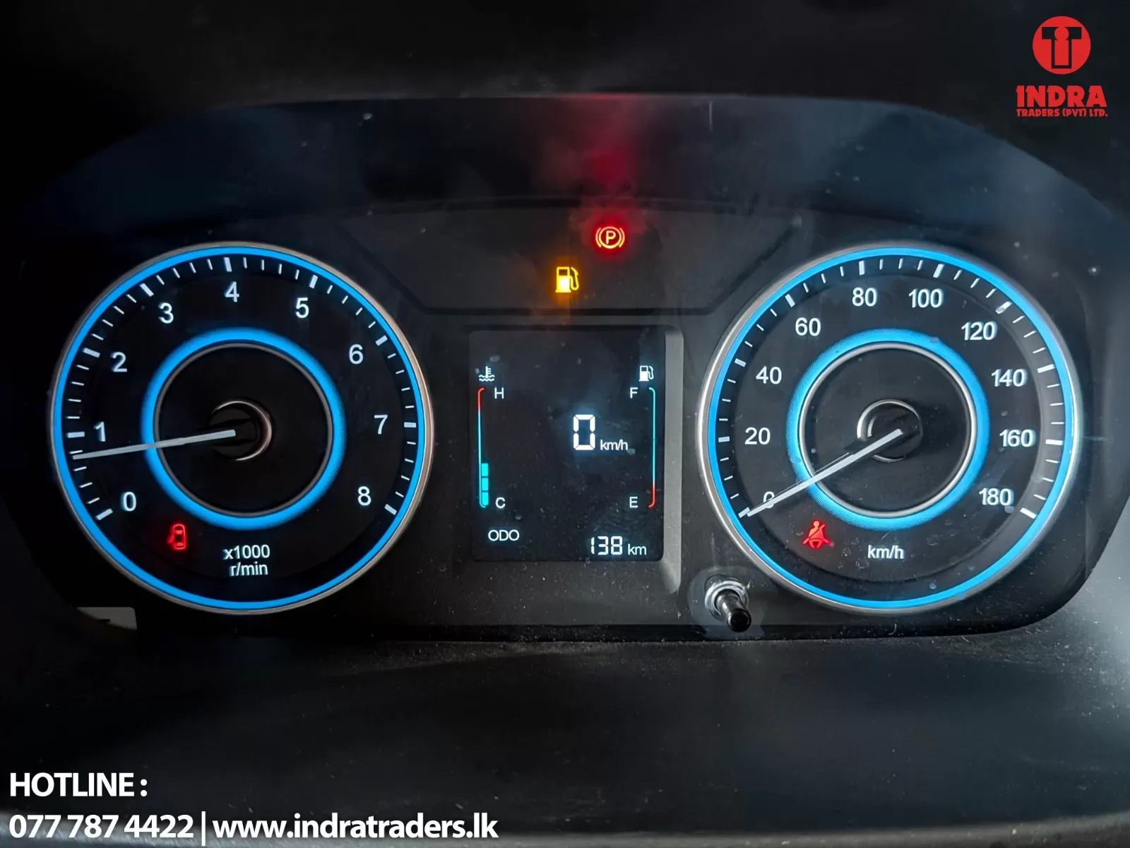 Car instrument cluster showing 0 km/h with tachometer on left, speedometer on right, central digital readout and warning lights (seatbelt, parking brake).
