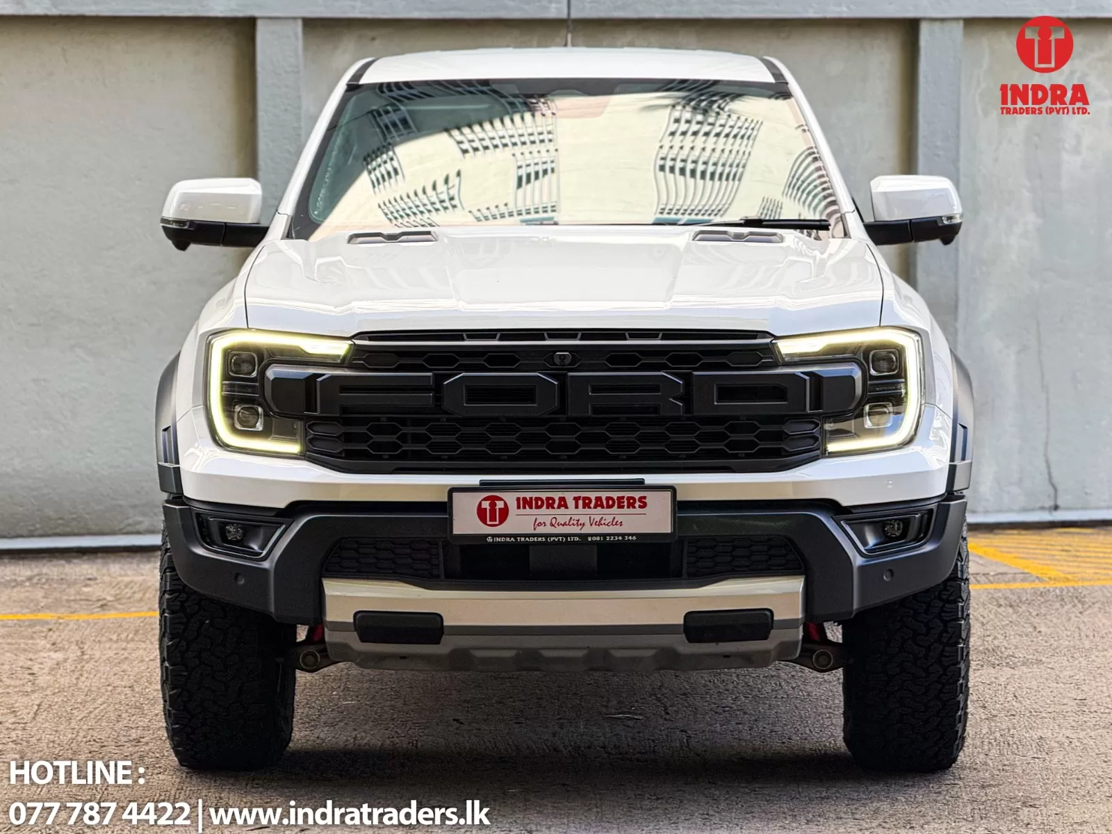 Front view of a white pickup truck with a bold black grille and LED headlights; Indra Traders branding appears in the top-right corner and contact info along the bottom edge.