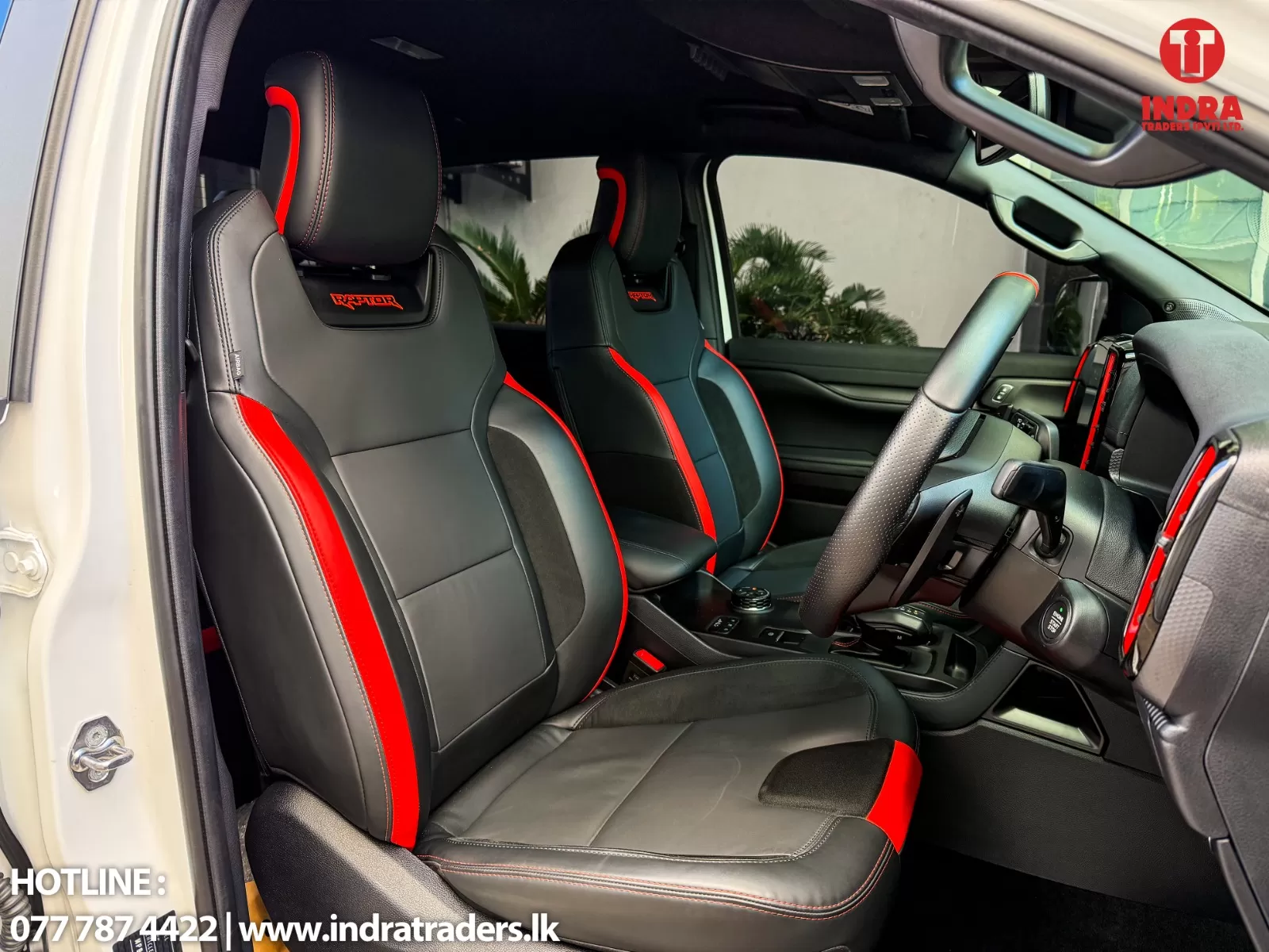 Car interior with black leather sport seats and red accents; steering wheel, center console, and dashboard visible in daylight.