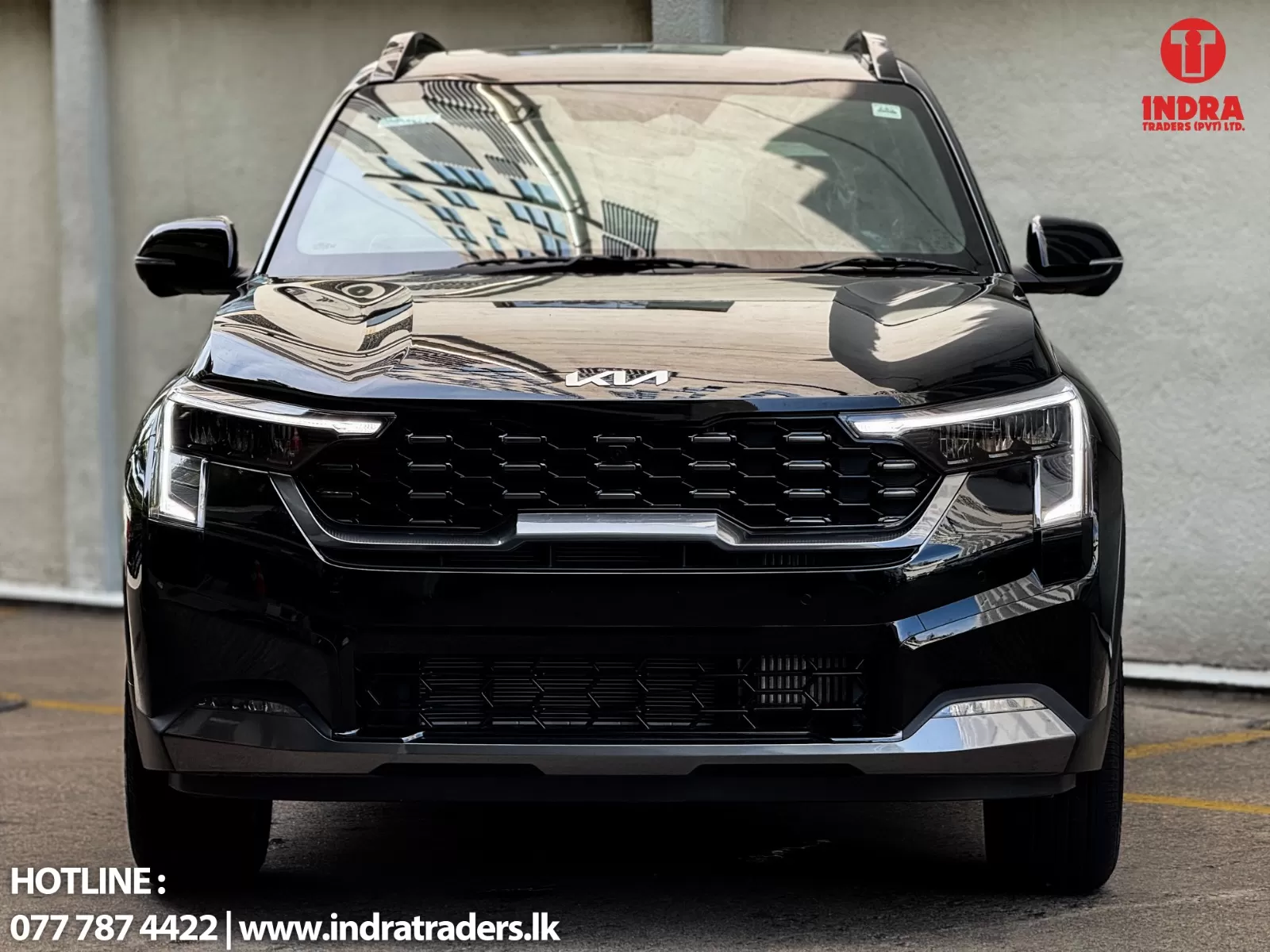 Front view of a black Kia SUV displaying chrome grille and headlights, with Indra Traders logo in the top-right and contact text at the bottom left.