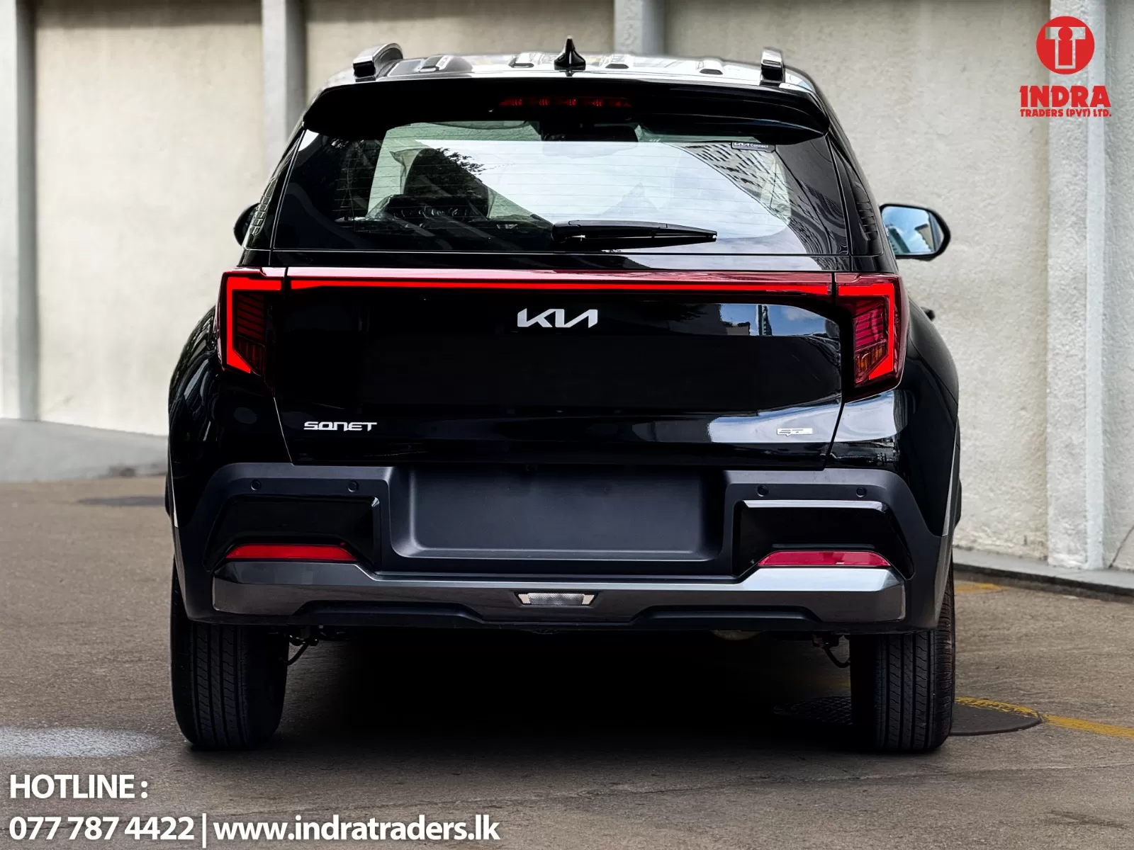 Rear view of a glossy black Kia Sonet SUV parked indoors; Indra Traders logo in the top-right corner and contact text at bottom-left reading HOTLINE: 077 787 4422 | www.indratraders.lk