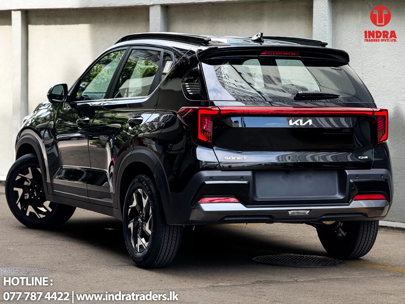 Black Kia Sonet SUV, rear three-quarter view; Indra Traders logo in top-right corner and hotline text bottom-left.