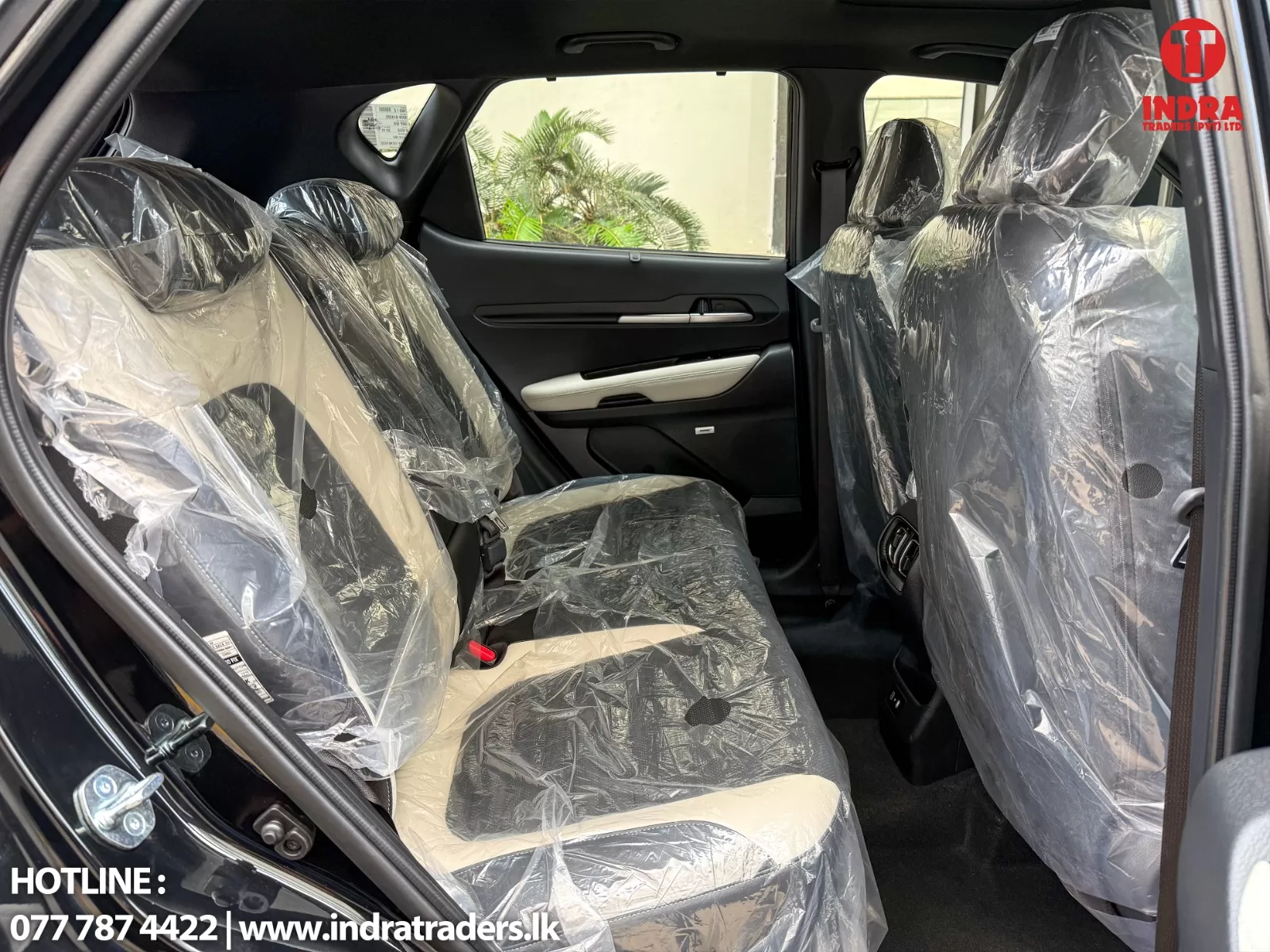Rear cabin of a new car with all seats wrapped in plastic, showing beige upholstery and black trim; door panel visible, dealership logo in the top-right corner.