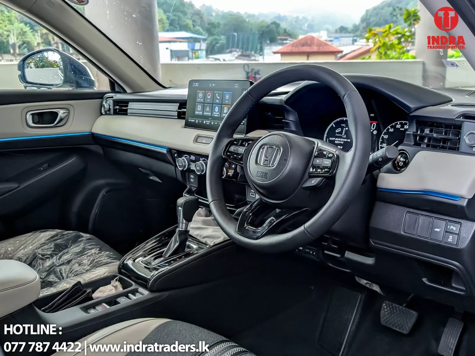 Interior view of a modern Honda car cabin with a large central touchscreen, digital gauges, and leather steering wheel; gear selector and climate controls visible; Indra Traders logo on the upper right.