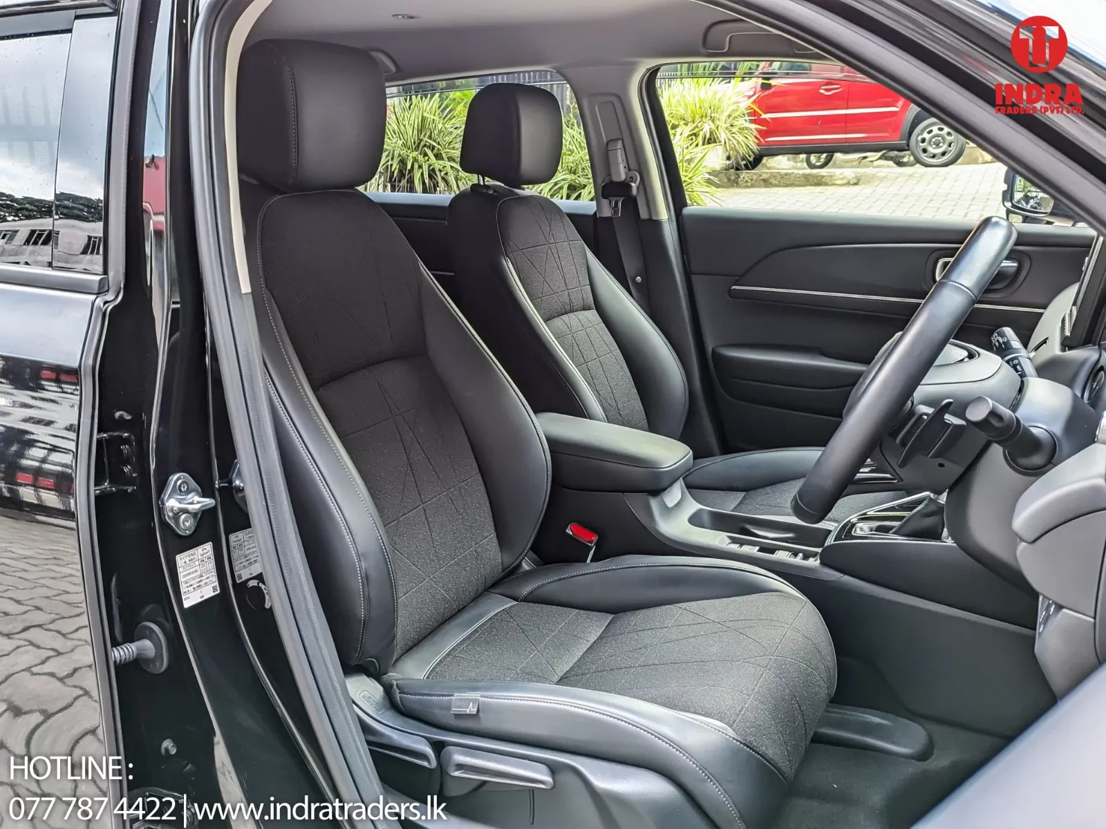 Right-hand-drive car interior with black fabric seats, center console, and steering wheel visible through the open driver-side door.