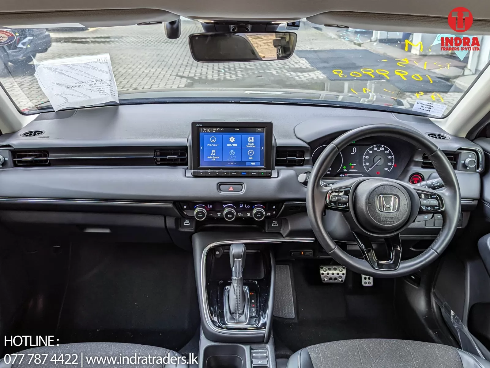 Front cabin of a modern Honda car: center touchscreen display, steering wheel with controls, automatic gear shifter, and climate controls visible on the dashboard.