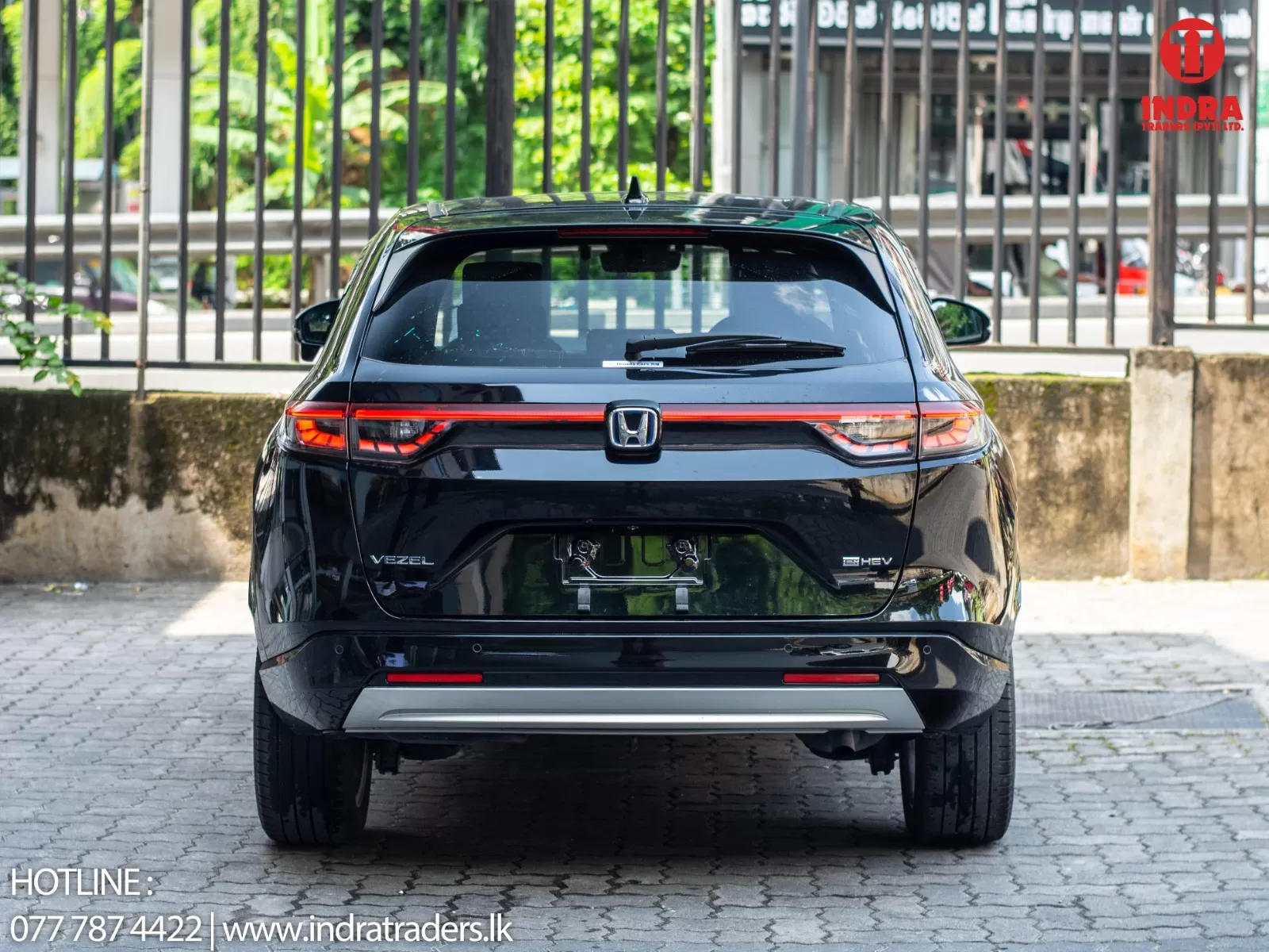 Rear view of a black Honda Vezel e:HEV parked on a cobblestone lot with red taillights and dealership watermark in the corner.