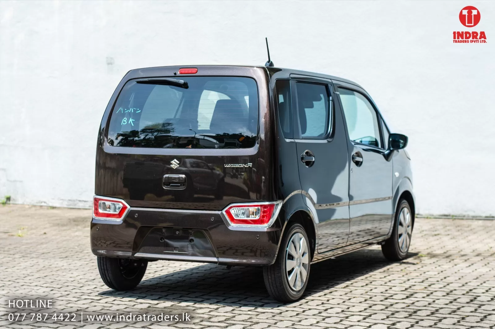 Rear and right-side view of a brown Suzuki WagonR parked on a cobblestone lot, with the Indra Traders logo in the top-right corner.