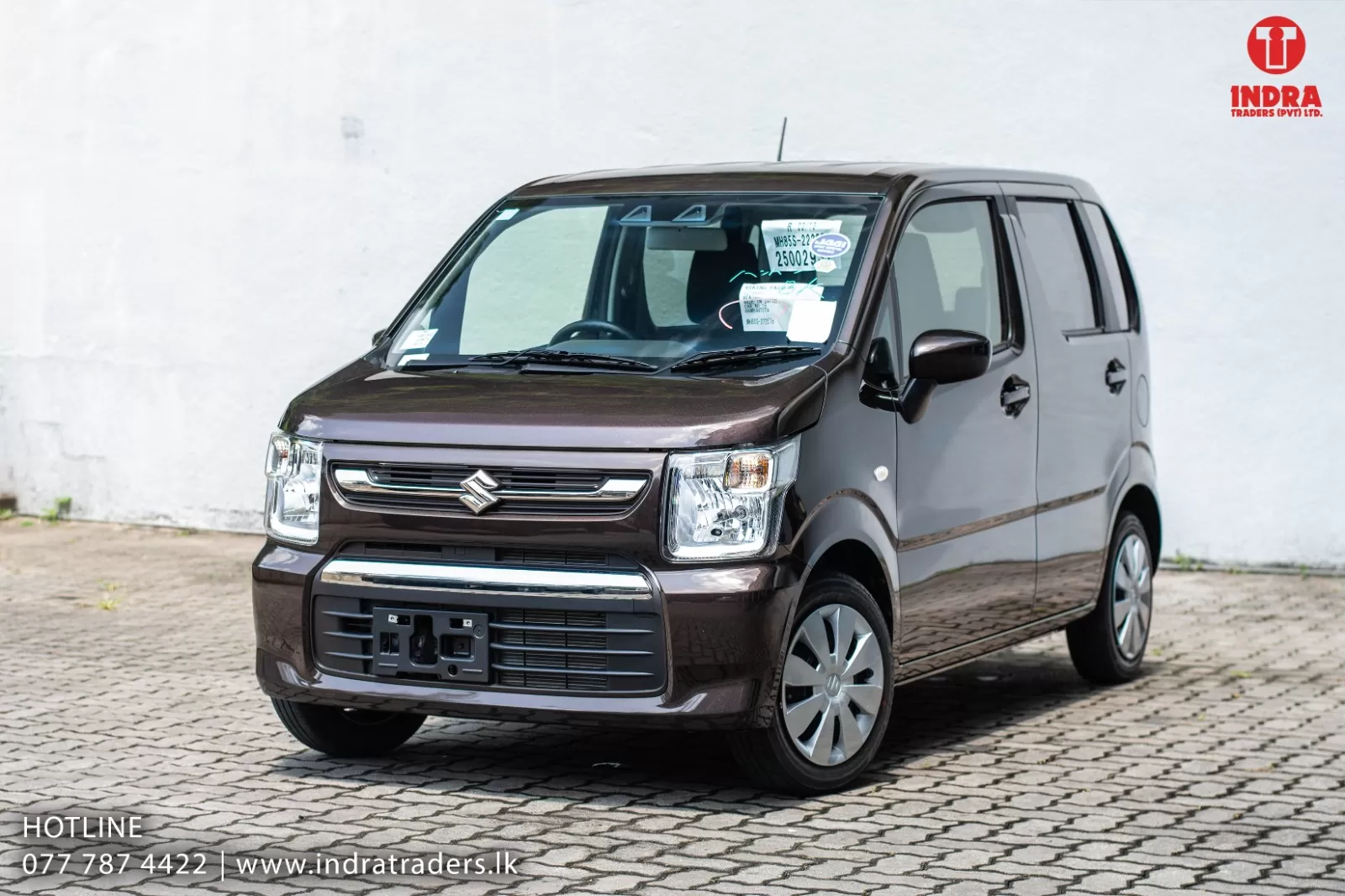 Brown Suzuki compact van parked on a brick lot; dealership logo at top-right and contact info at bottom-left.