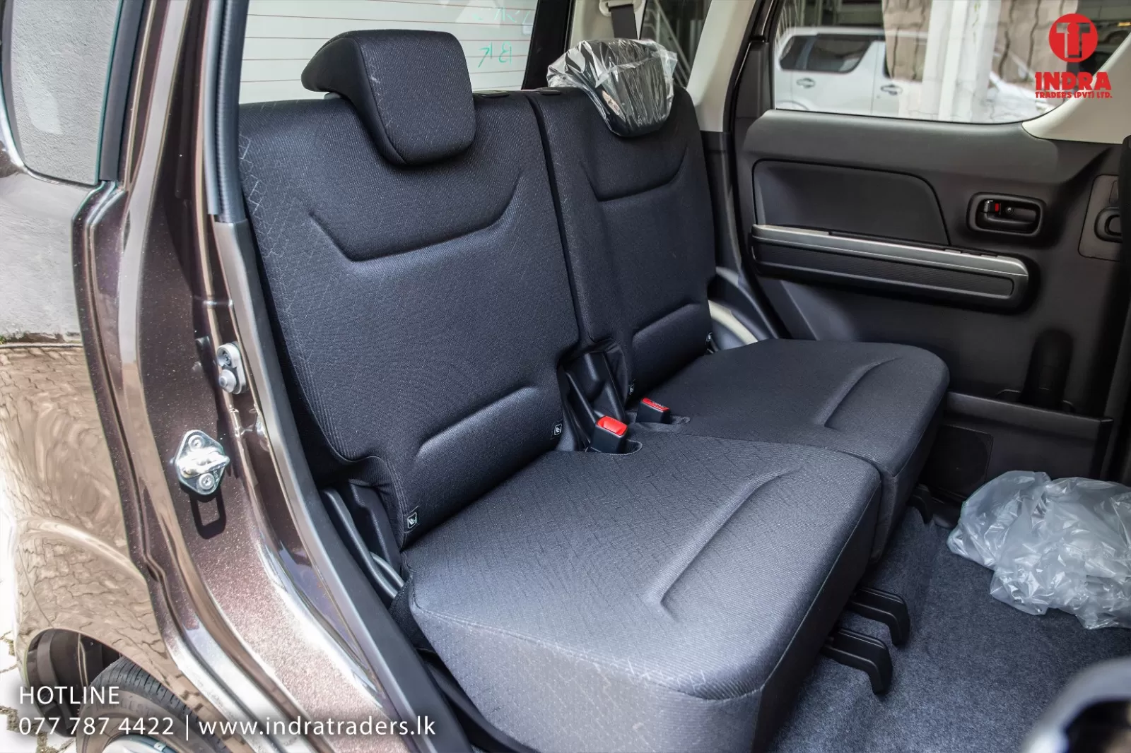 Rear bench seat of a dark gray SUV with two seats, headrests, and red seatbelt buckles; a plastic bag sits on the floor by the door.