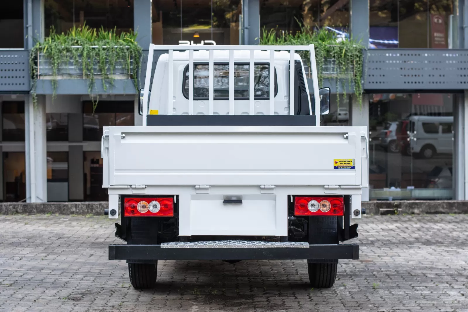 Rear view of a white flatbed truck with a cargo bed and red taillights in a paved parking area.