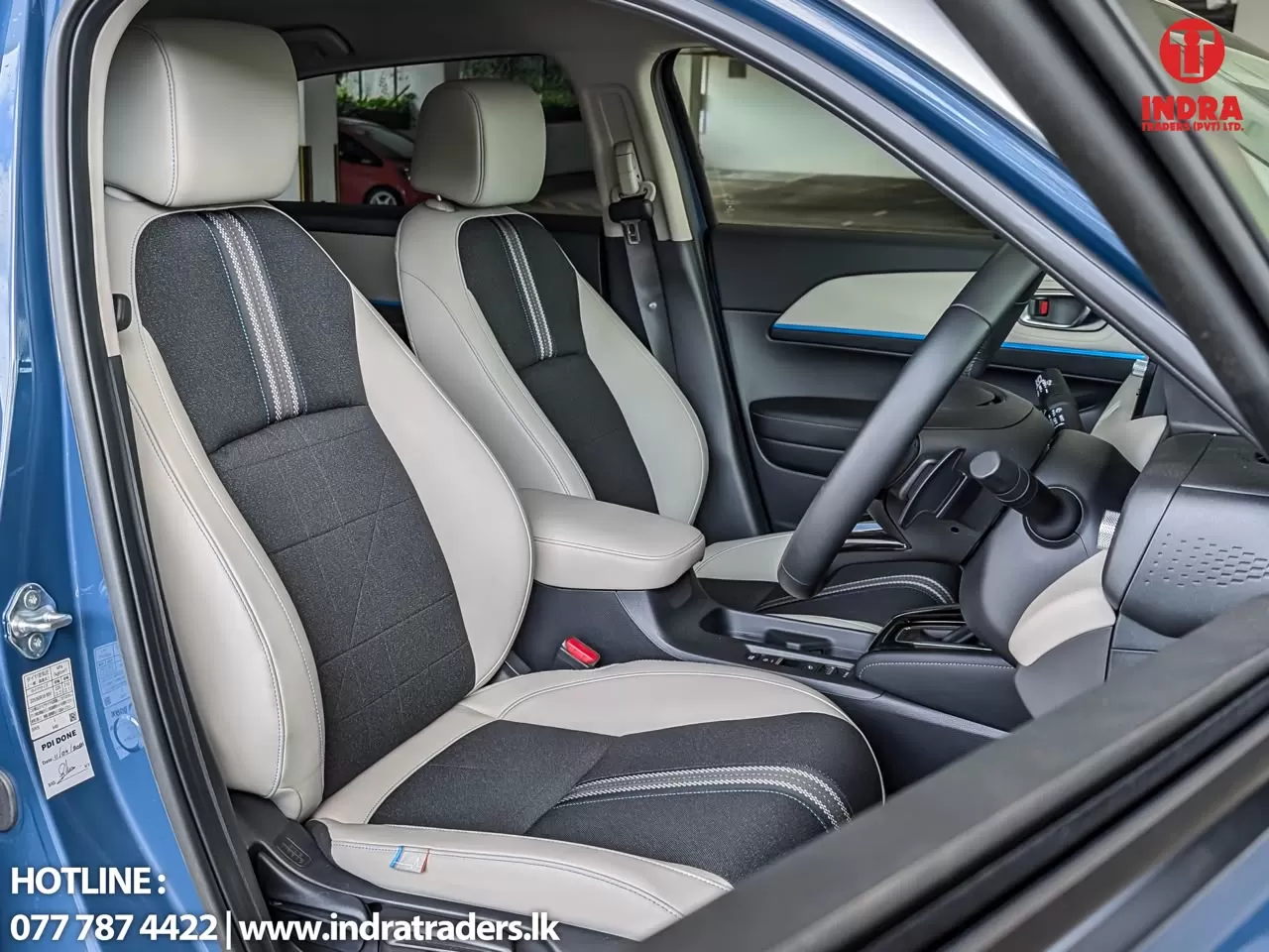 Two-tone front car seats in gray and black with a center console and steering wheel, door open on the left side; Indra Traders logo in the top-right corner.