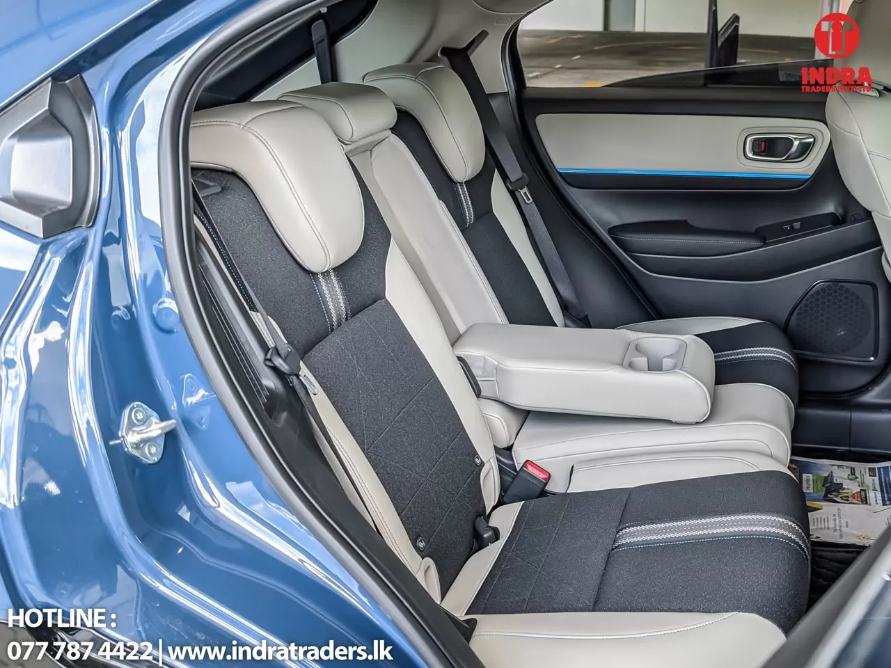 Rear passenger seat area of a blue SUV featuring beige and black two-tone upholstery, a fold-down center armrest with cupholders, visible seat belts, and a door panel with a blue accent line.
