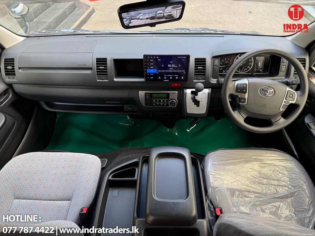 Right-hand-drive car interior featuring steering wheel on the right, central touchscreen, climate controls, and front seats viewed from the center console.