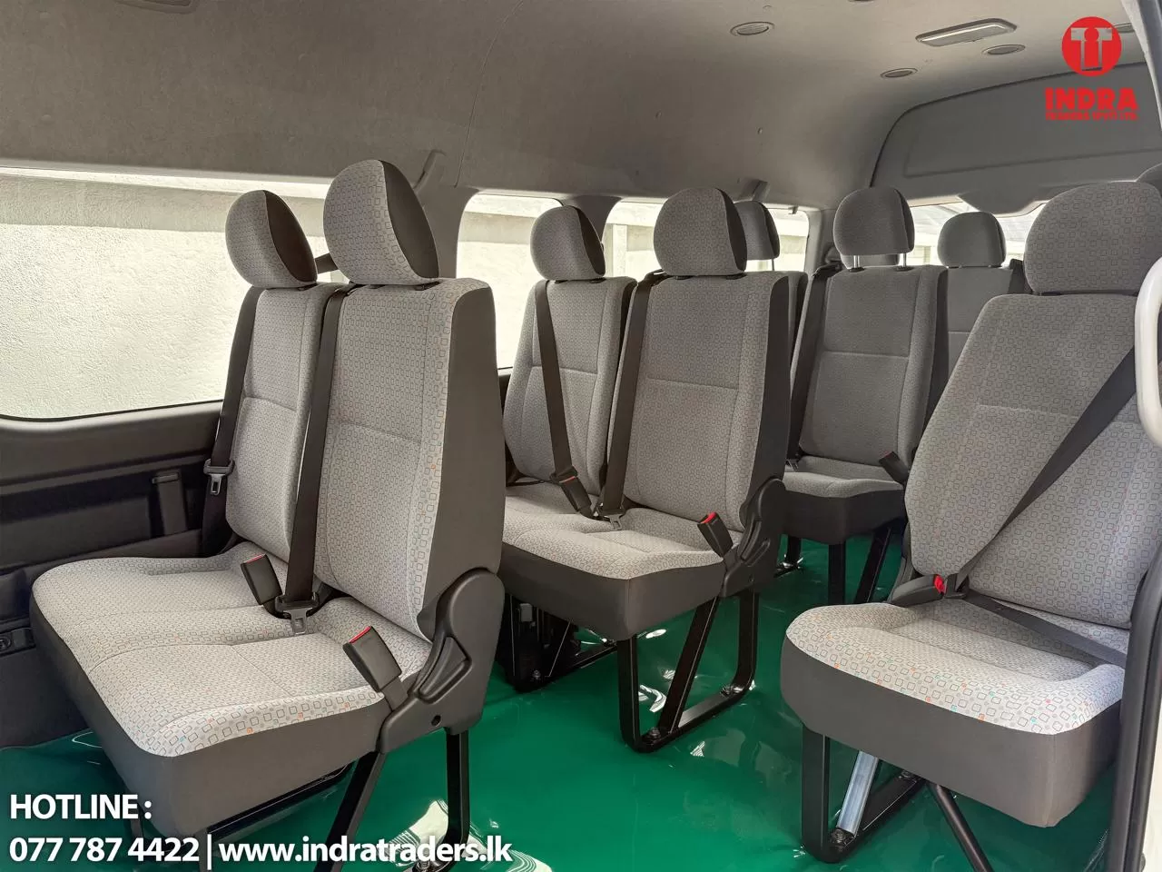 Interior of a grey passenger van with multiple rows of patterned seats and seat belts, green floor visible