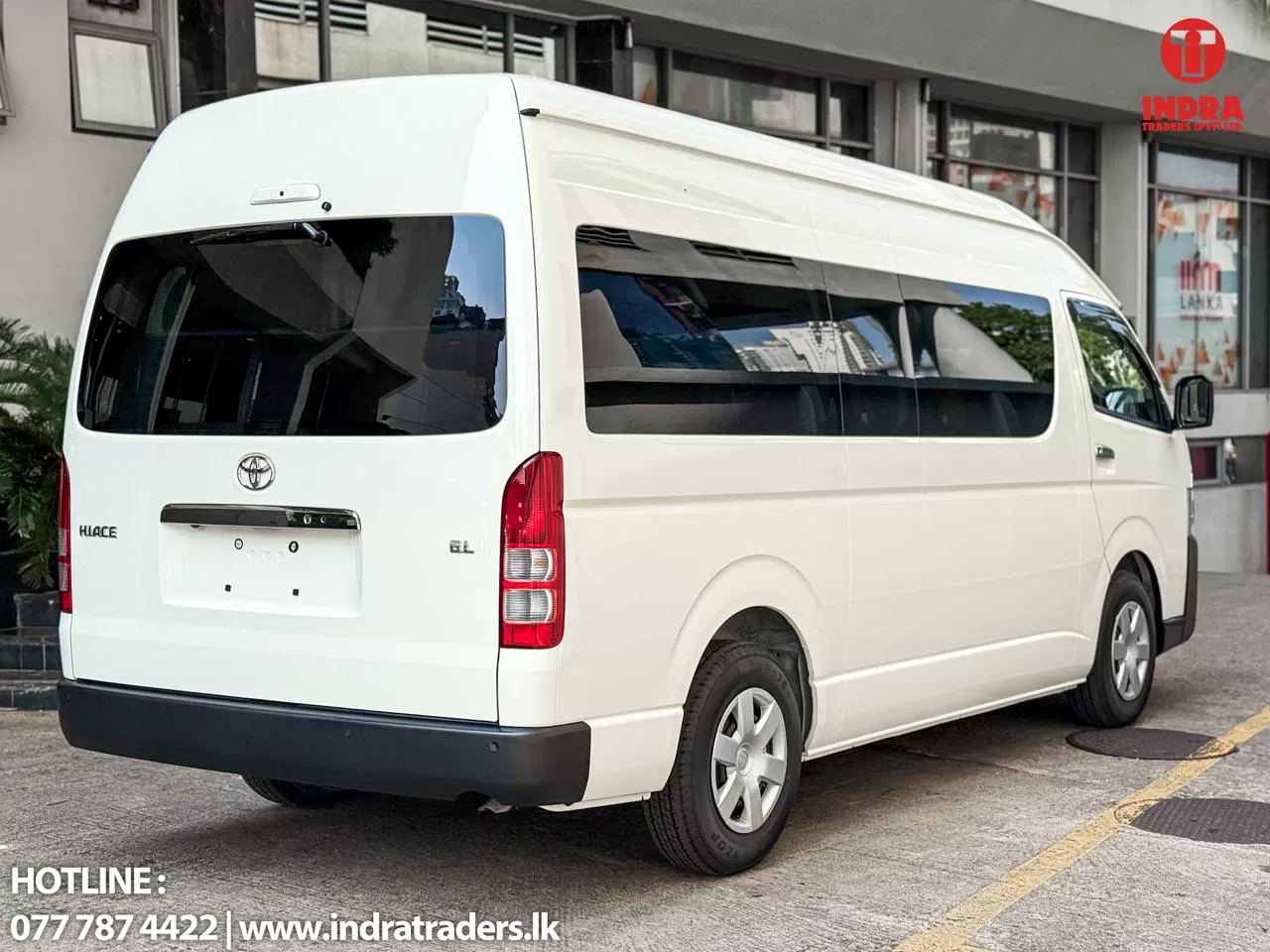 White Toyota Hiace GL van parked on a city street, showing the rear and passenger side with a visible Indra Traders logo in the top-right corner and hotline text at the bottom-left.