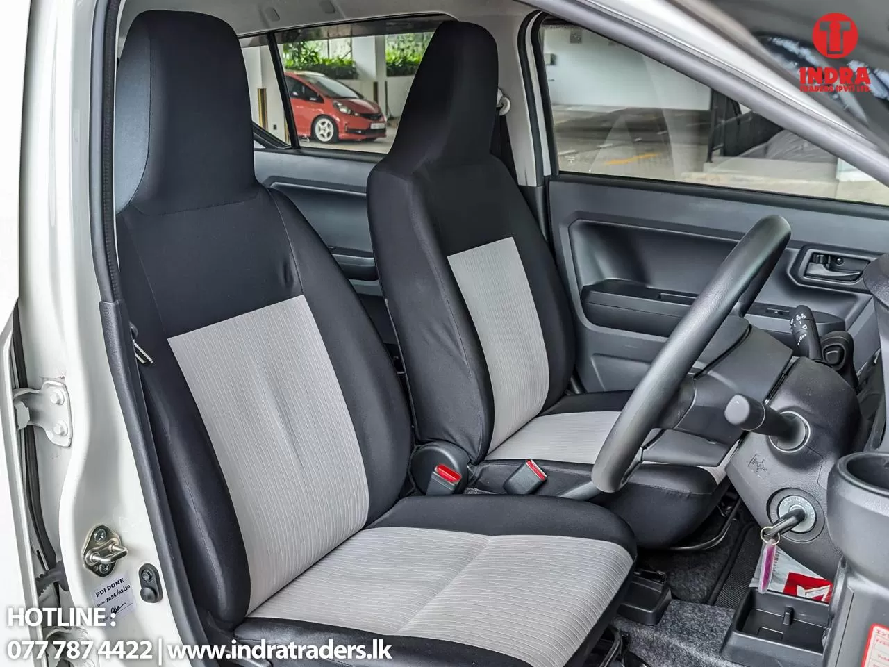 Right-hand-drive car interior featuring the steering wheel and two front seats with gray fabric upholstery.