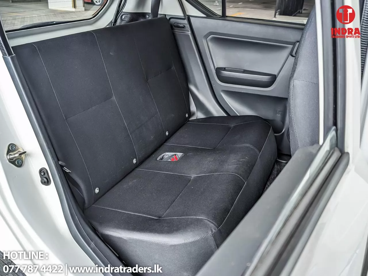Rear car bench seat in black fabric with door panel and visible seat belt buckle; open car door on the left shows the interior.