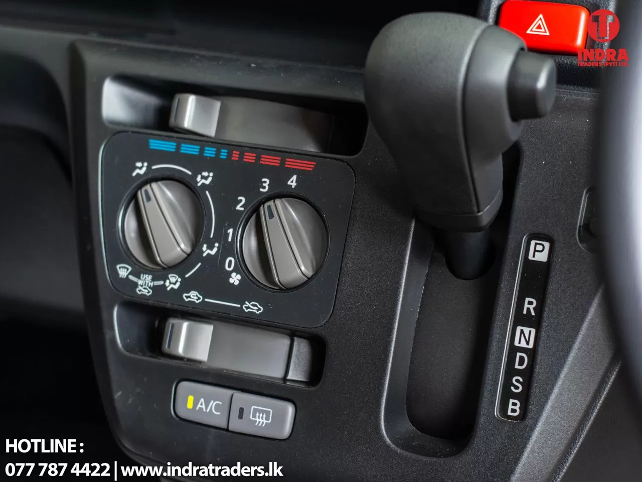 Car climate control panel with two dials and orange/red temperature indicators, plus a gear selector to the right and an A/C button at the bottom (informational image).