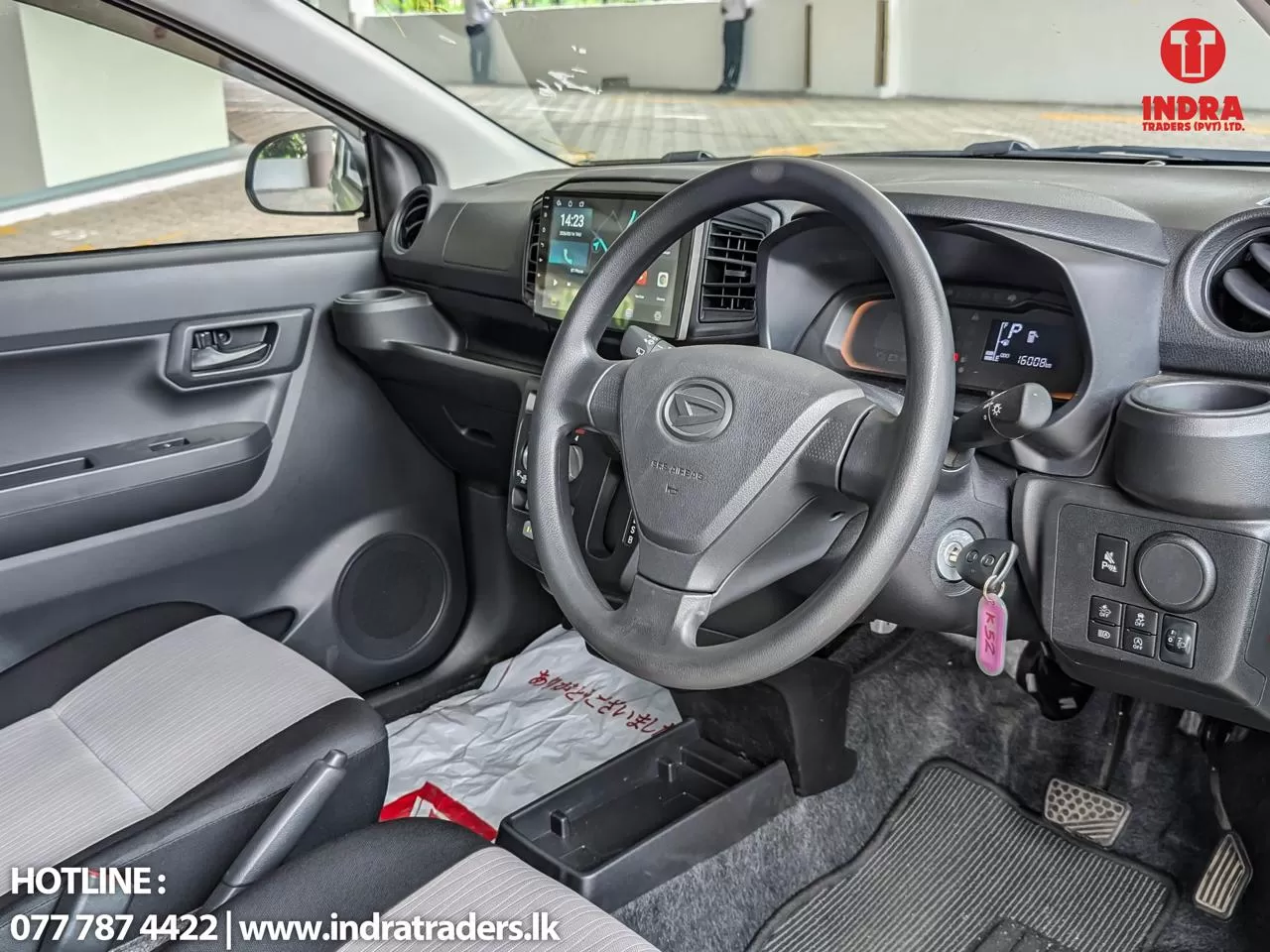 Interior of a gray compact car: steering wheel, touchscreen dashboard, and driver’s side controls visible with a key in the ignition; Indra Traders watermark.