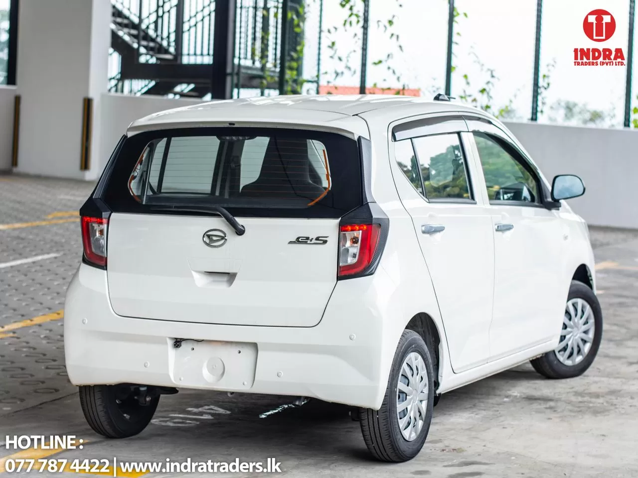 White compact hatchback parked in a lot, shown from the rear-left; Indra Traders logo visible in the top-right corner.